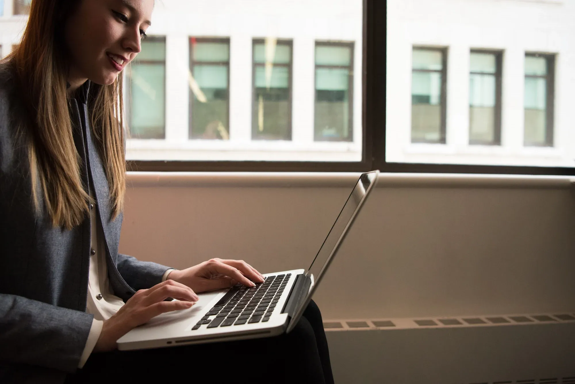 A person using a laptop by a window; illustrative stock photograph.
