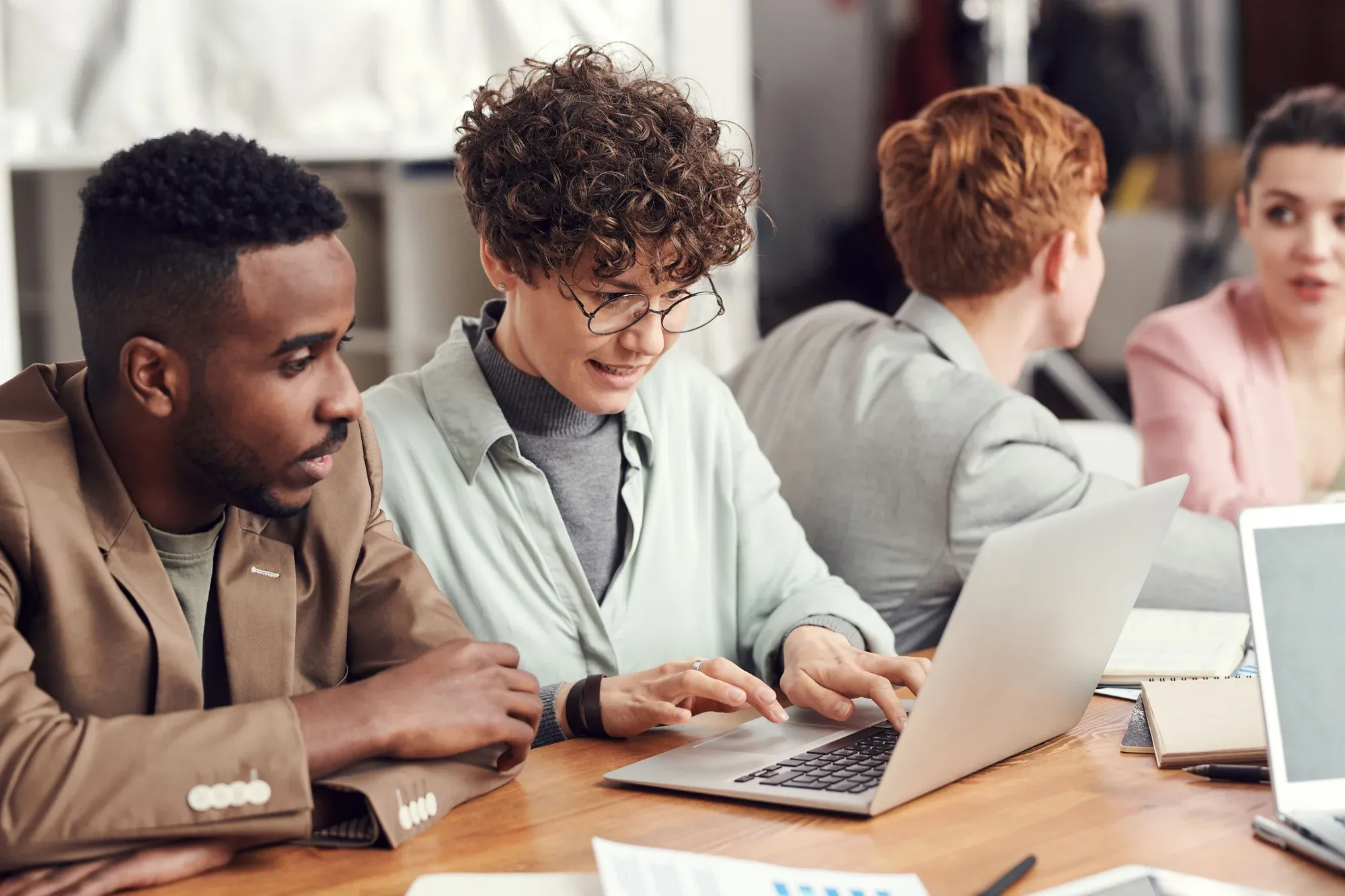 People learning and collaborating around laptops at a table; illustrative stock photograph.